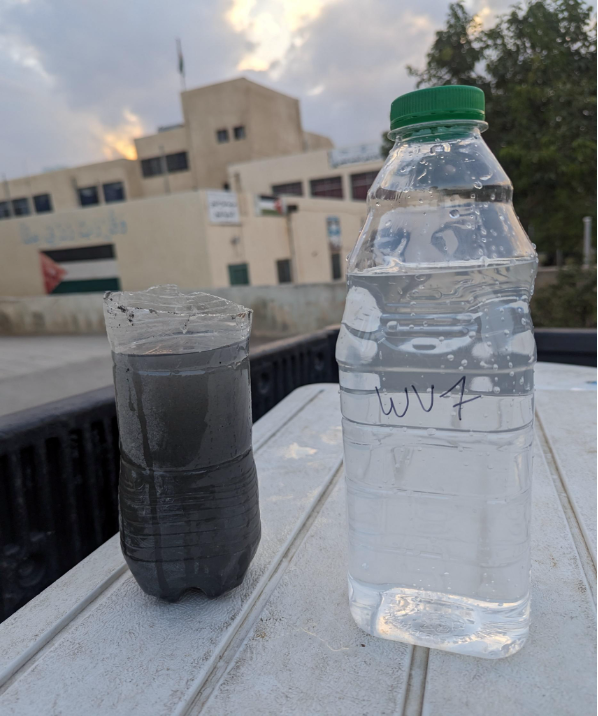 Two water samples on a truck bed: one bottle containing clear water and another cut plastic bottle holding dark, muddy water for comparison.